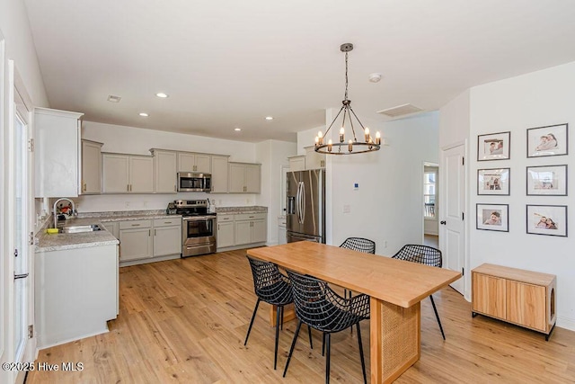 kitchen with pendant lighting, sink, gray cabinets, stainless steel appliances, and light hardwood / wood-style floors