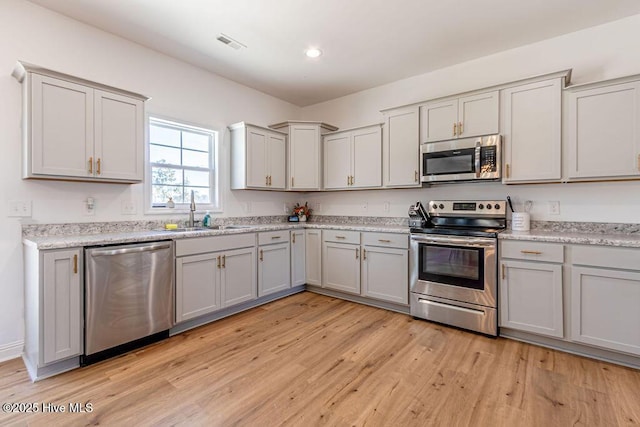 kitchen with stainless steel appliances, light stone countertops, sink, and light wood-type flooring