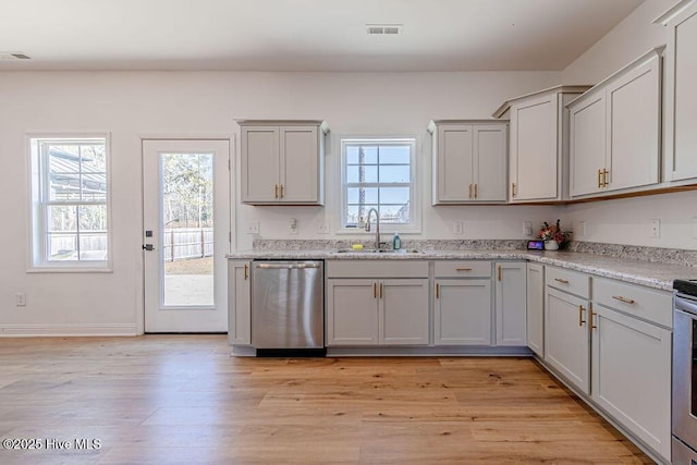 kitchen with light stone counters, light hardwood / wood-style floors, dishwasher, and sink