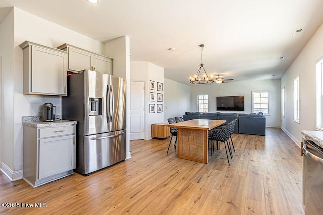 kitchen with gray cabinetry, light stone counters, light hardwood / wood-style floors, stainless steel appliances, and an inviting chandelier