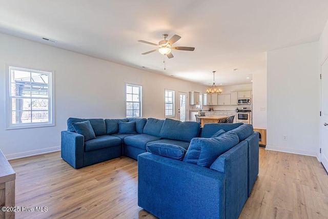 living room with ceiling fan with notable chandelier and light hardwood / wood-style flooring