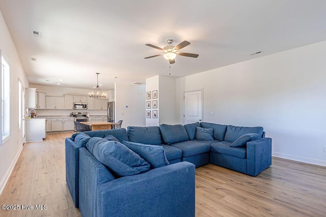 living room featuring ceiling fan with notable chandelier and light wood-type flooring