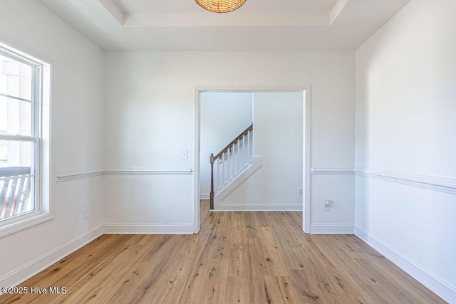 empty room with a tray ceiling and light hardwood / wood-style flooring