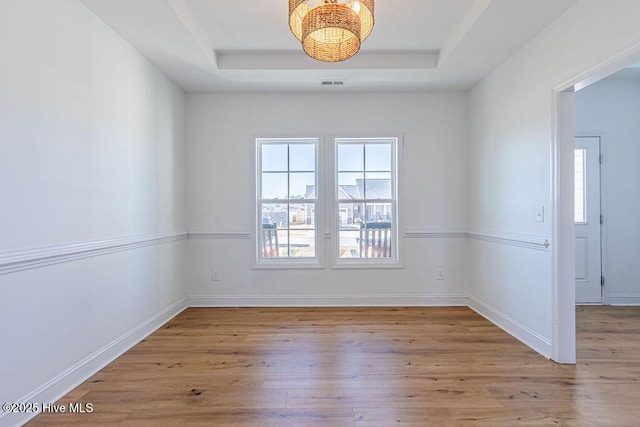 empty room featuring a tray ceiling and light hardwood / wood-style flooring