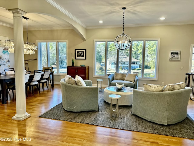 living room featuring hardwood / wood-style flooring, crown molding, a chandelier, and ornate columns