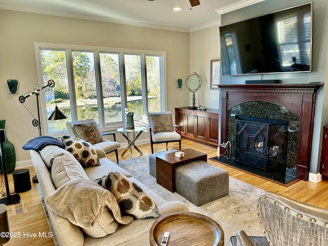 living room featuring ceiling fan, light wood-type flooring, a high end fireplace, and crown molding