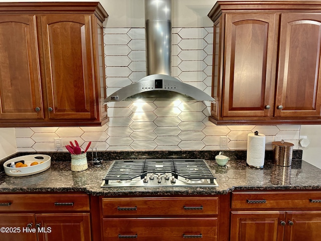 kitchen with stainless steel gas stovetop, wall chimney exhaust hood, dark stone countertops, and backsplash