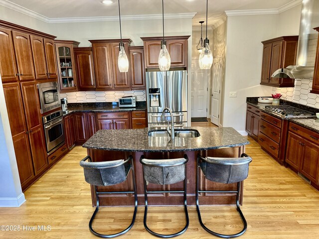 kitchen with a center island with sink, decorative backsplash, sink, light hardwood / wood-style flooring, and appliances with stainless steel finishes