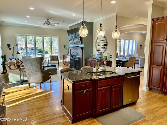 kitchen with decorative light fixtures, dark stone countertops, sink, light hardwood / wood-style flooring, and an island with sink