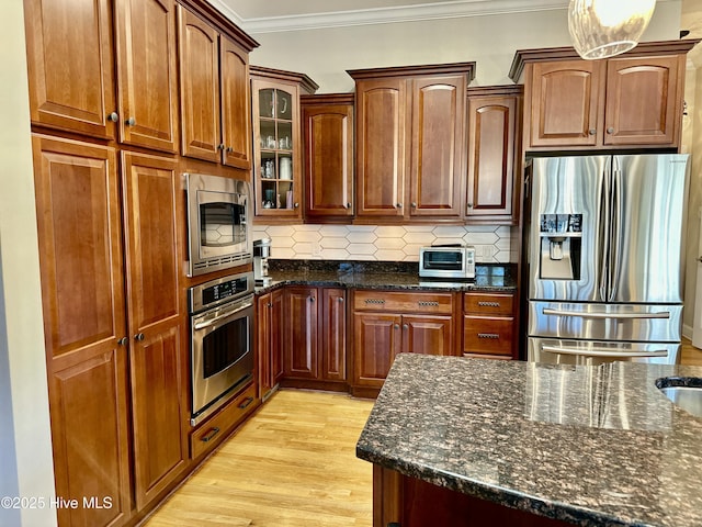 kitchen with tasteful backsplash, dark stone countertops, light hardwood / wood-style floors, crown molding, and stainless steel appliances