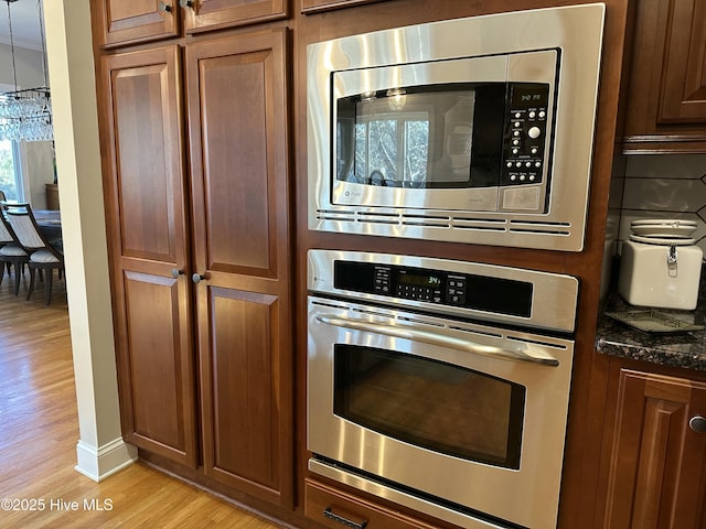 kitchen with appliances with stainless steel finishes, dark stone counters, light hardwood / wood-style floors, backsplash, and hanging light fixtures