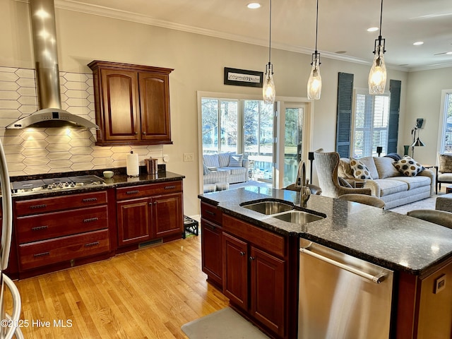 kitchen featuring wall chimney range hood, stainless steel appliances, light hardwood / wood-style floors, sink, and backsplash