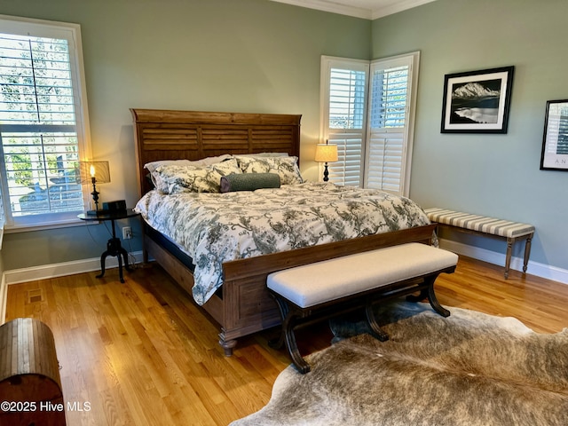 bedroom with light wood-type flooring, crown molding, and multiple windows