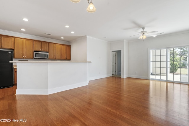 7195 Bonaventure St SW Apt 104, Ocean Isle Beach, NC 28469 - kitchen featuring stainless steel microwave, freestanding refrigerator, brown cabinets, light wood-style floors, and a ceiling fan