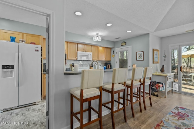 kitchen with white appliances, a textured ceiling, light brown cabinetry, a kitchen breakfast bar, and backsplash