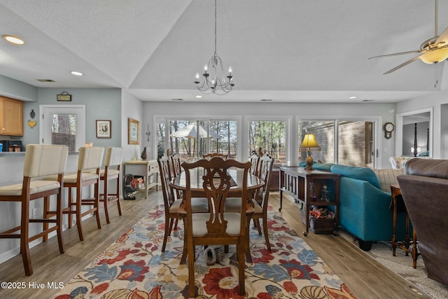 dining room with a textured ceiling, lofted ceiling, ceiling fan with notable chandelier, and light hardwood / wood-style flooring