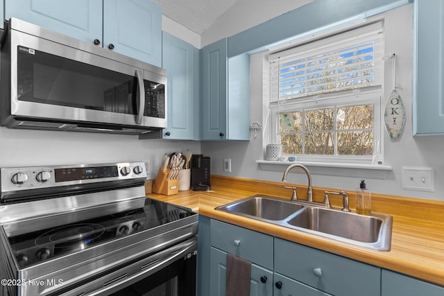 kitchen with blue cabinetry, stainless steel appliances, sink, and a textured ceiling