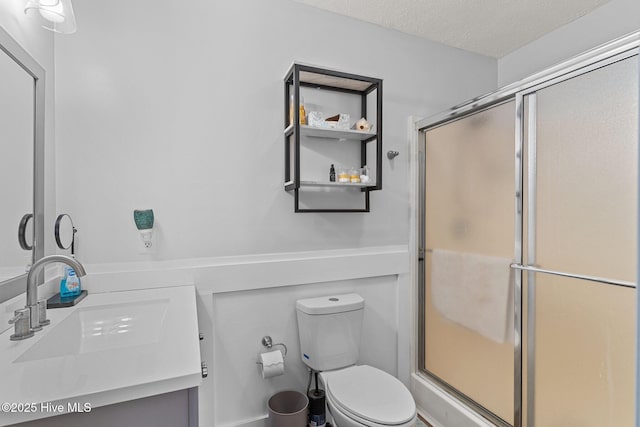 bathroom featuring vanity, toilet, a shower with door, and a textured ceiling