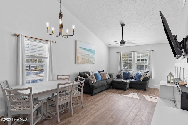 living room with lofted ceiling, ceiling fan with notable chandelier, wood-type flooring, and a textured ceiling