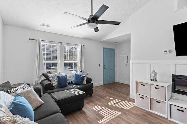 living room with lofted ceiling, hardwood / wood-style flooring, ceiling fan, a fireplace, and a textured ceiling