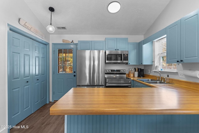 kitchen with vaulted ceiling, appliances with stainless steel finishes, kitchen peninsula, and decorative light fixtures