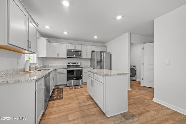 kitchen featuring washer / dryer, a sink, stainless steel appliances, light wood-type flooring, and a center island