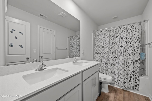 bathroom featuring double vanity, toilet, wood finished floors, and a sink