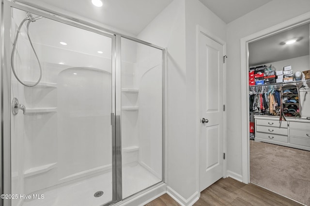 full bathroom featuring a stall shower, a walk in closet, and wood finished floors