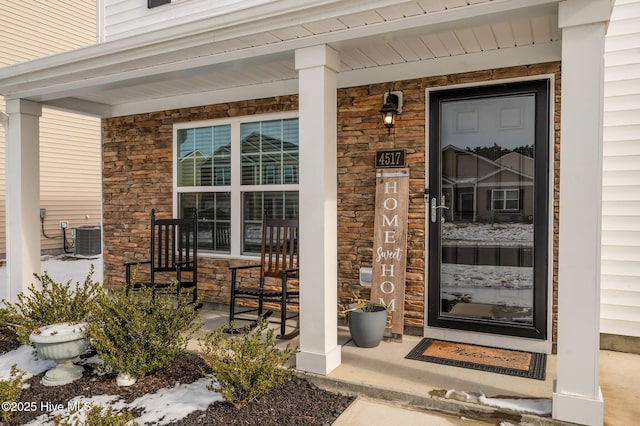 entrance to property featuring central AC unit, covered porch, and stone siding