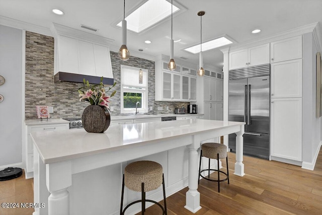 kitchen with a large island, built in refrigerator, white cabinetry, hanging light fixtures, and a skylight