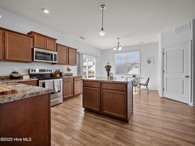 kitchen featuring pendant lighting, hardwood / wood-style floors, dark stone counters, and appliances with stainless steel finishes