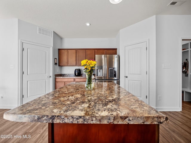 kitchen with dark wood-type flooring, stainless steel fridge, and a kitchen island