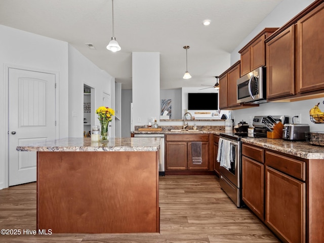 kitchen with decorative light fixtures, sink, a center island, stainless steel appliances, and light hardwood / wood-style flooring