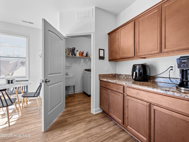 kitchen featuring light stone counters, washer / dryer, and light wood-type flooring