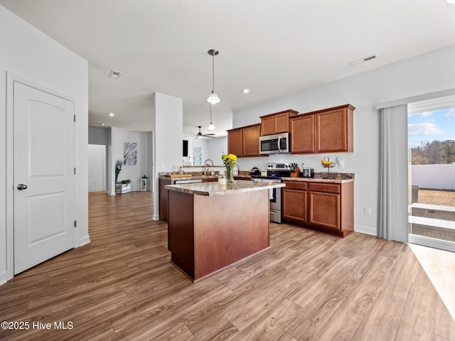 kitchen with pendant lighting, wood-type flooring, sink, stainless steel appliances, and light stone countertops