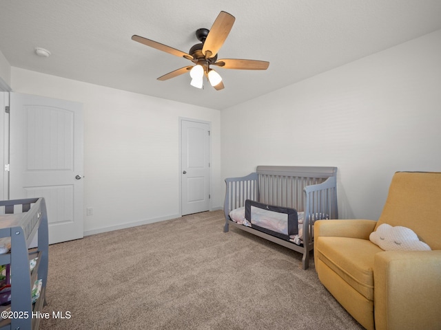 carpeted bedroom featuring a crib and ceiling fan