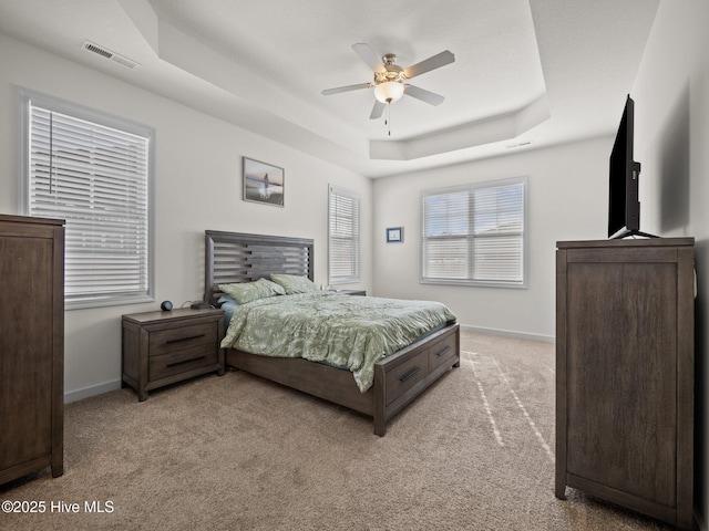 bedroom featuring light carpet, a tray ceiling, and ceiling fan