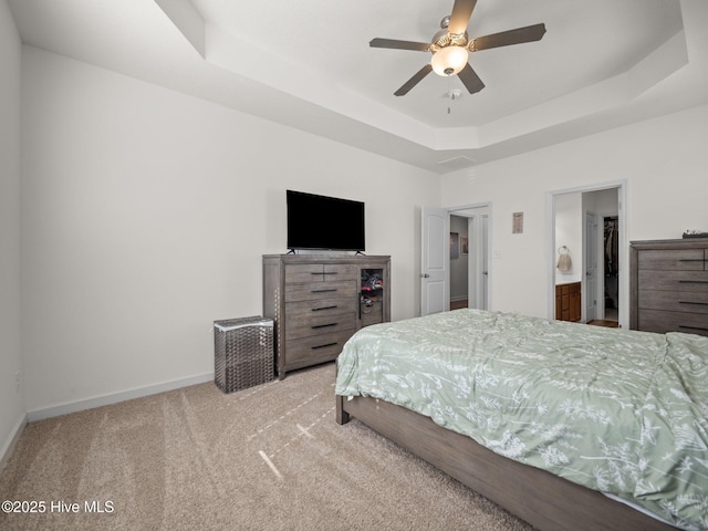 bedroom with connected bathroom, a tray ceiling, light colored carpet, and ceiling fan