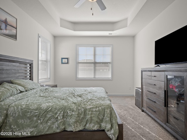 carpeted bedroom with ceiling fan, a tray ceiling, and multiple windows