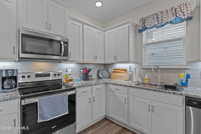 kitchen with stainless steel appliances, white cabinetry, light stone countertops, and sink