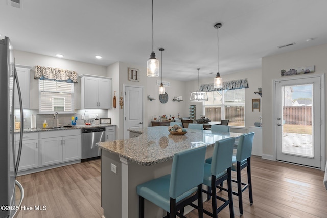 kitchen with appliances with stainless steel finishes, white cabinetry, sink, a center island, and light stone countertops