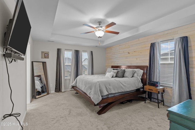 bedroom featuring a tray ceiling, wooden walls, light colored carpet, and ceiling fan