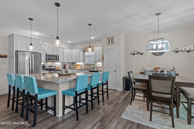 kitchen featuring appliances with stainless steel finishes, a breakfast bar, decorative light fixtures, white cabinets, and dark hardwood / wood-style flooring