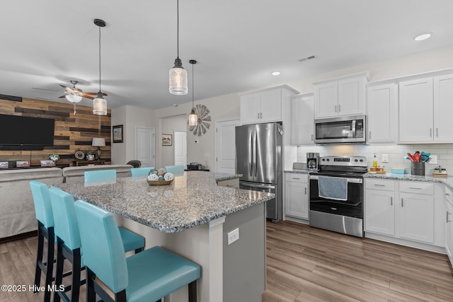 kitchen featuring appliances with stainless steel finishes, a center island, white cabinets, a kitchen bar, and decorative light fixtures