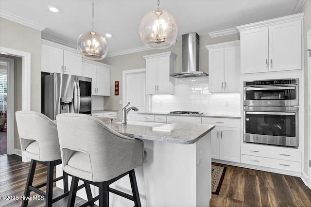 kitchen featuring white cabinetry, appliances with stainless steel finishes, a center island with sink, and wall chimney range hood