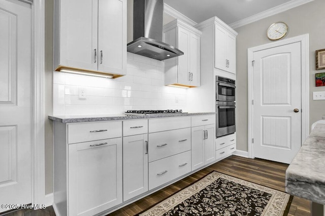 kitchen with appliances with stainless steel finishes, white cabinets, crown molding, dark wood-type flooring, and wall chimney exhaust hood