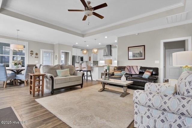 living room with a tray ceiling, ornamental molding, ceiling fan, and light wood-type flooring