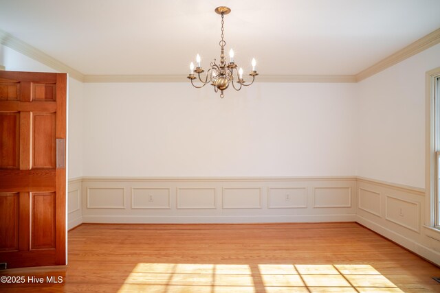 unfurnished room with a notable chandelier, ornamental molding, and light wood-type flooring