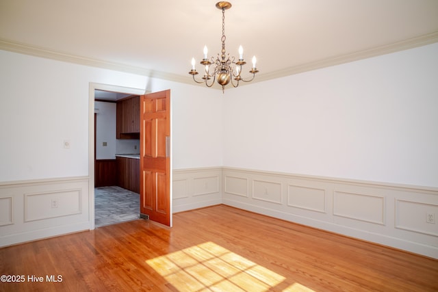 spare room with a notable chandelier, crown molding, and wood-type flooring