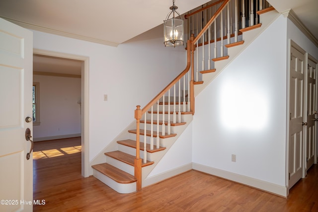 staircase featuring crown molding, wood-type flooring, and an inviting chandelier